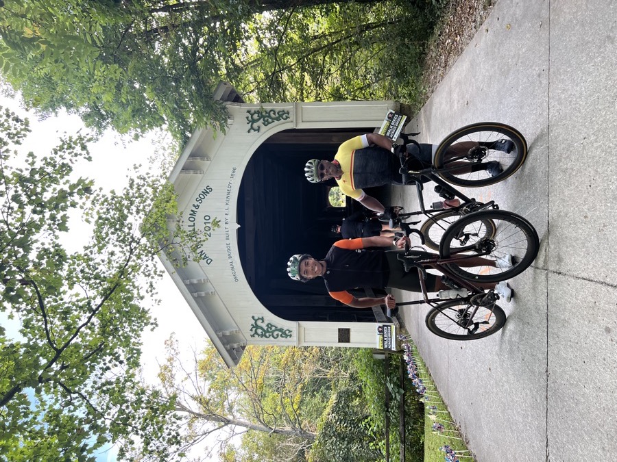 Benian and a riding buddy holding their bikes in front of a covered bridge