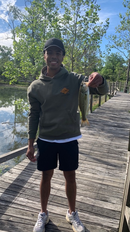 Benian holding a freshly caught bass on a lake boardwalk